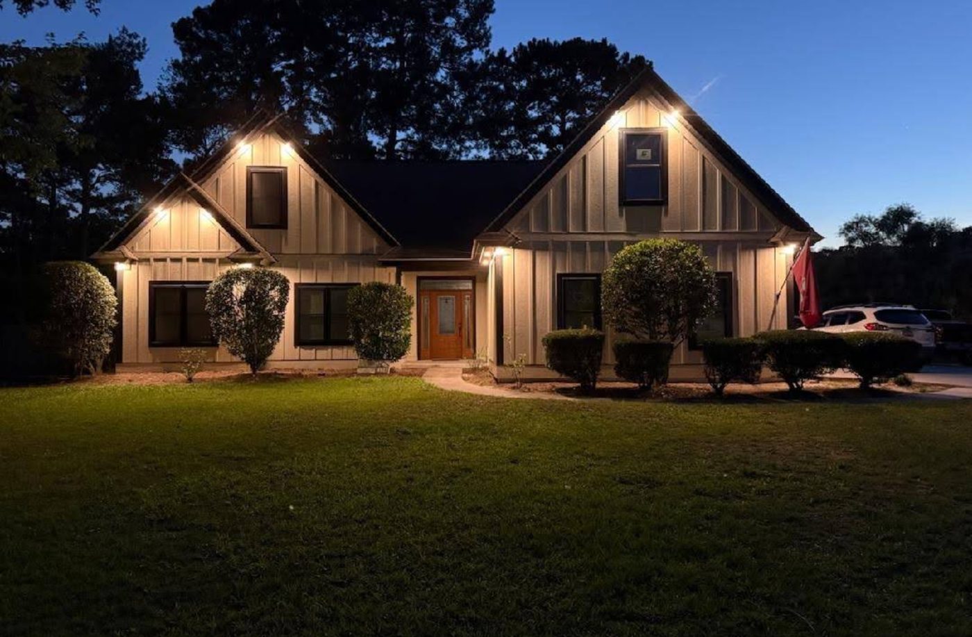Single-storey home photographed at dusk with soffit downlights and accent lighting switched on