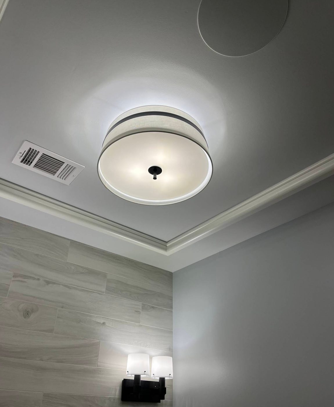 Drum flush-mount ceiling light and a two-lamp vanity sconce in a tiled bathroom