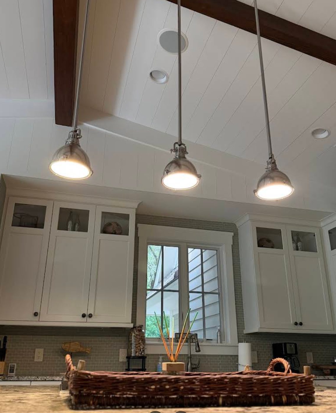 Three metal pendant lights over a kitchen counter beneath a vaulted shiplap ceiling with recessed downlights