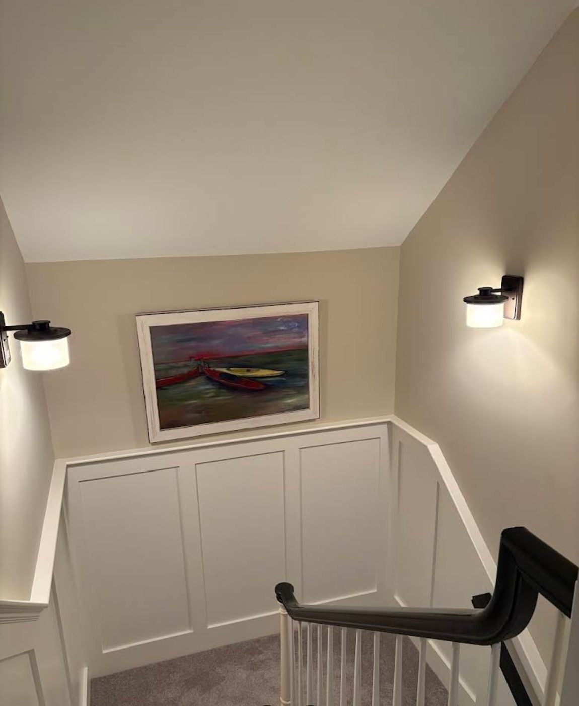 Two wall sconces flanking framed artwork above panelled wainscoting on a stair landing